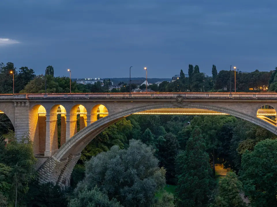 The Pont Adolphe in Luxembourg at dusk, its stone arches lit above the Pétrusse valley